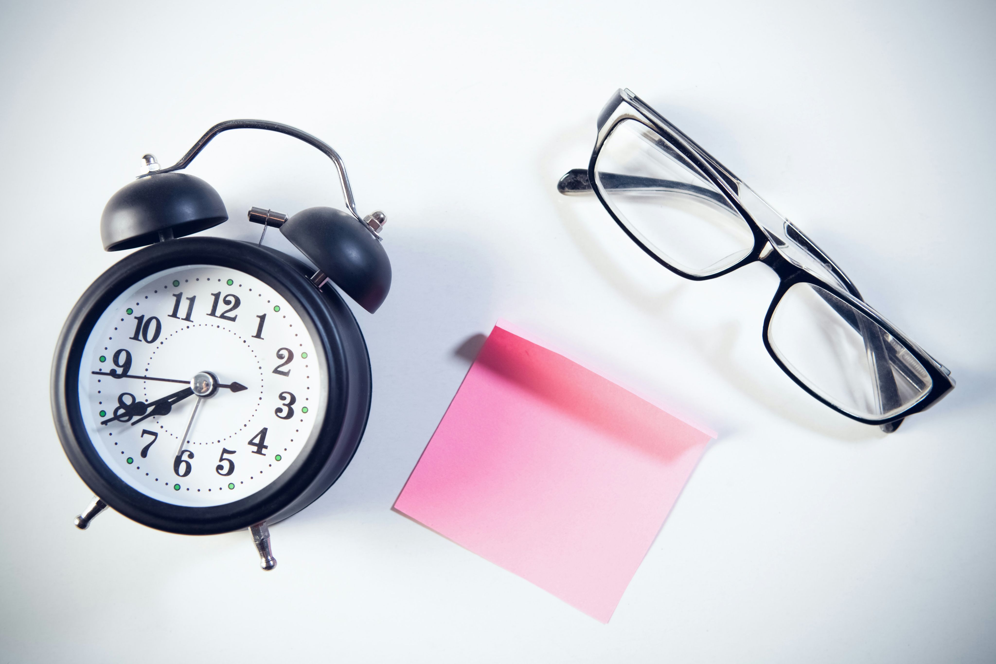 Alarm clock, glasses, and pink sticky note on white.