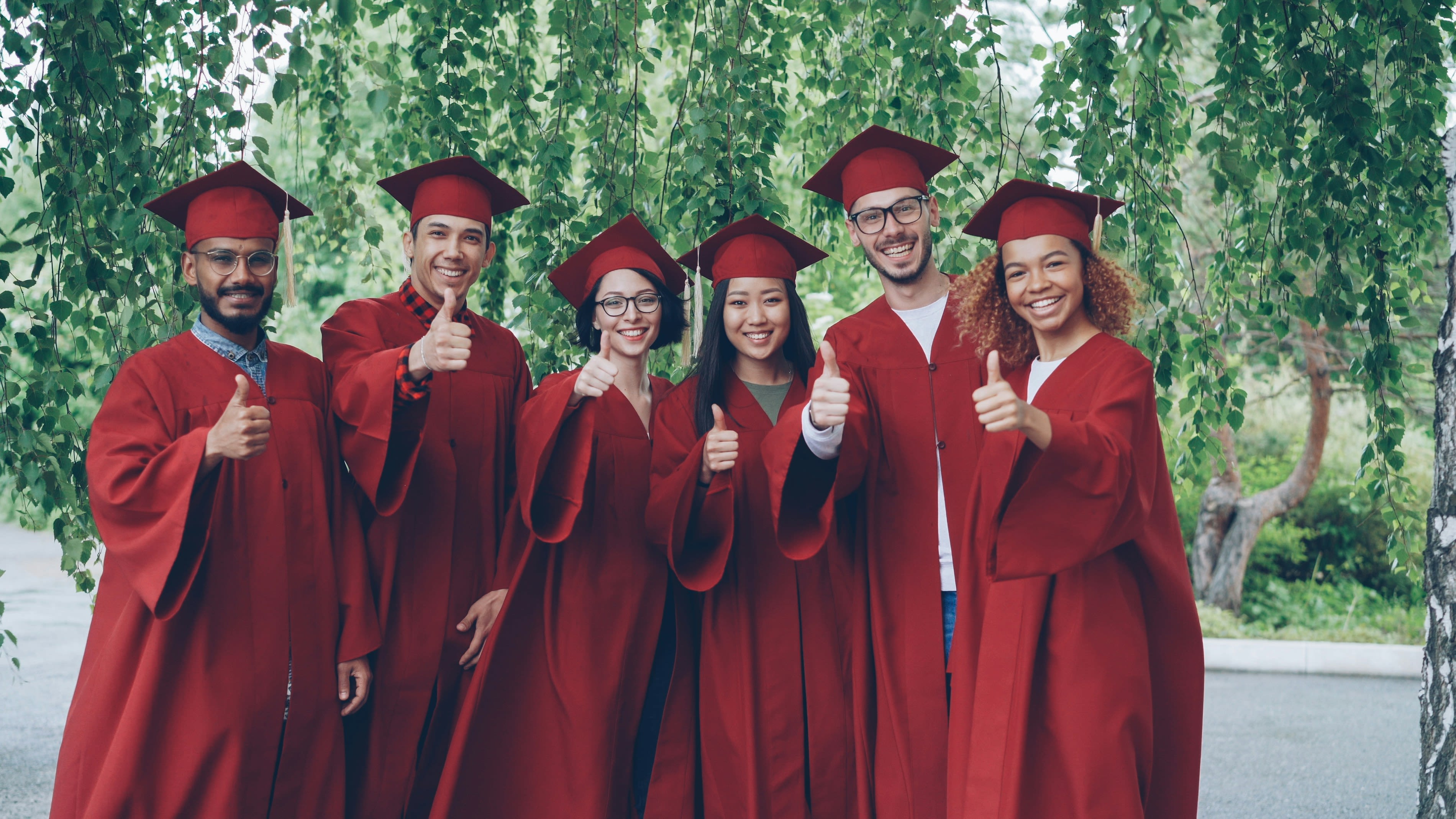 Six graduates in red gowns give thumbs up