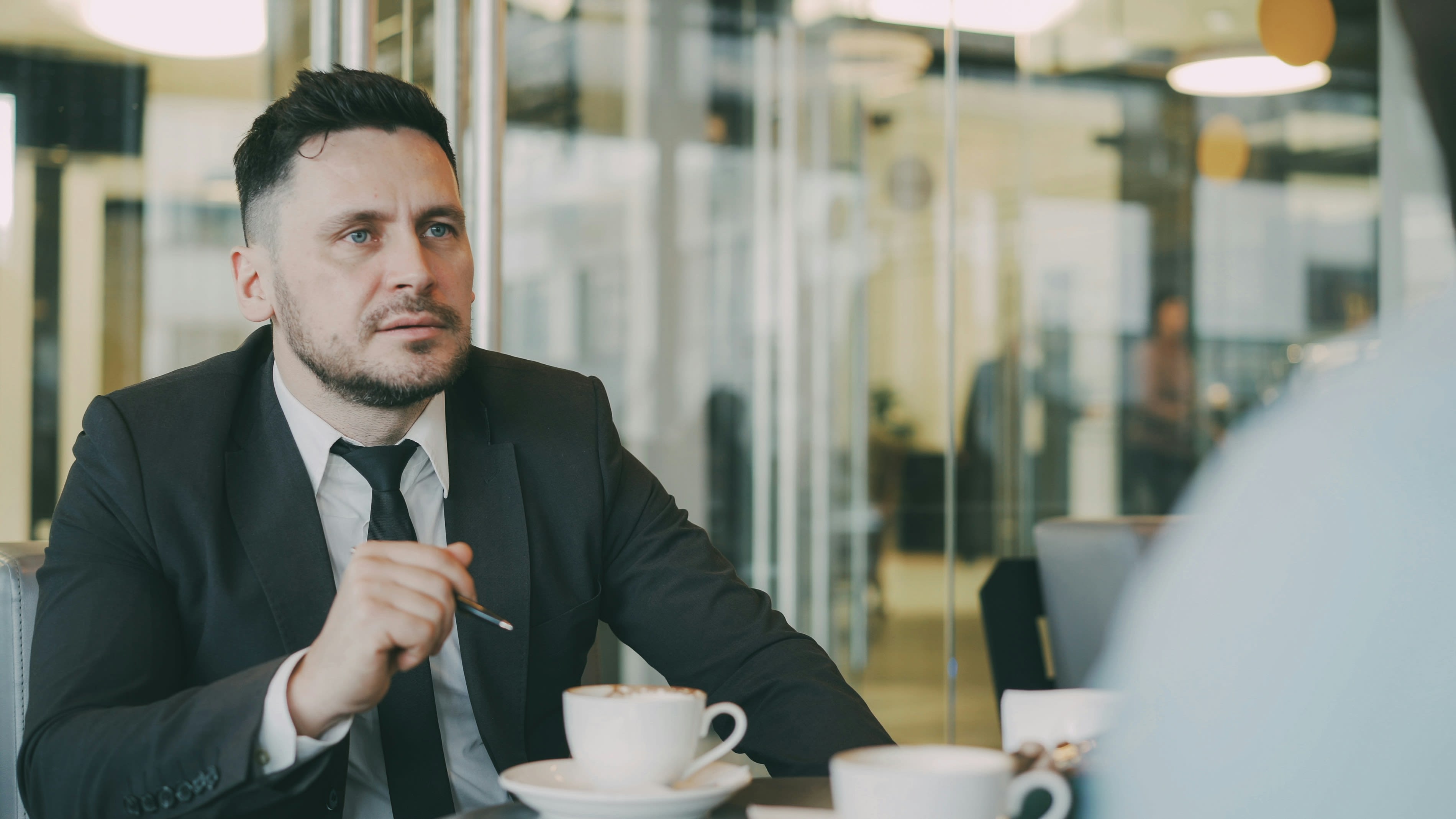Man in suit talks at table with coffee cups.