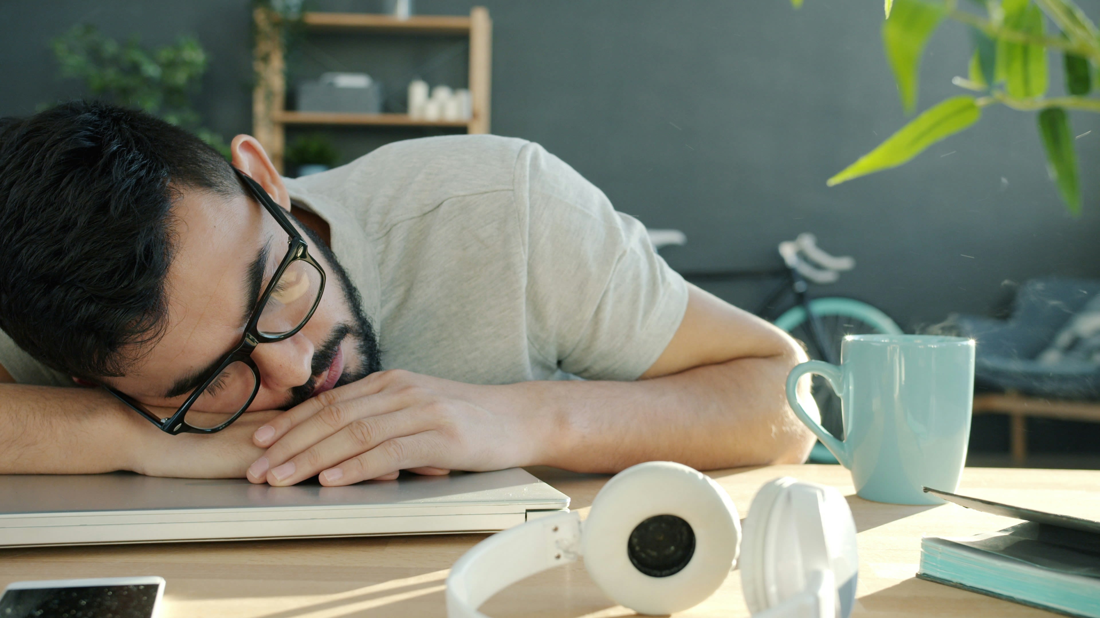 Man sleeping at desk with headphones and coffee.